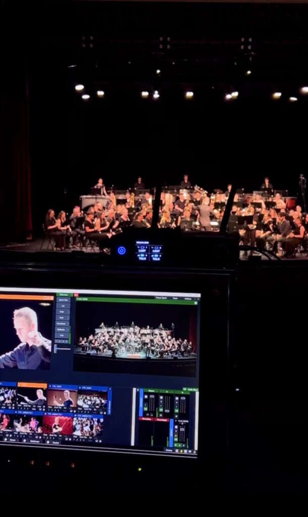 Ecran de captation en premier plan et l'orchestre en second pour la prestation d'un orchestre d'étudiants